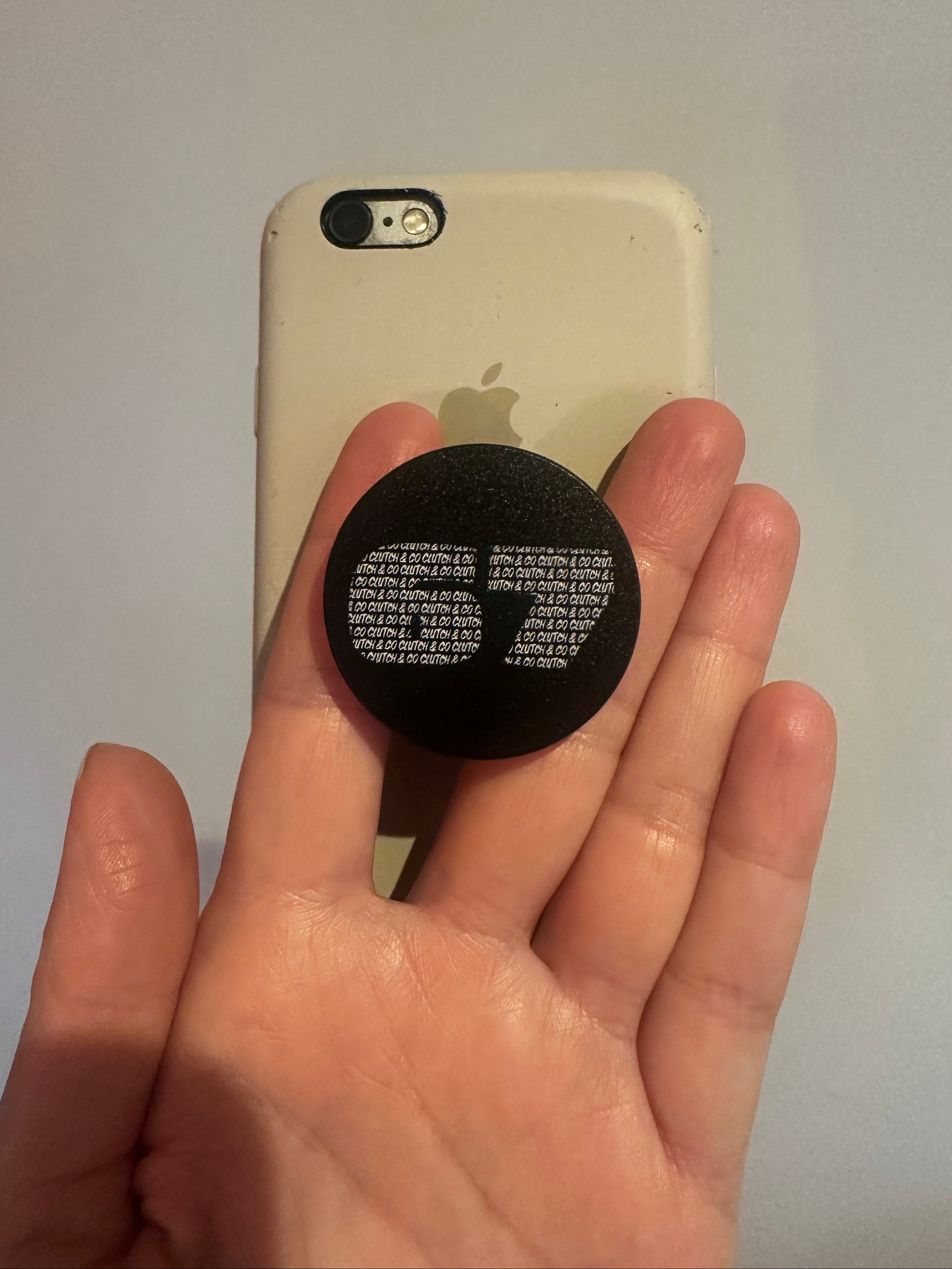 Hand holding a black pop socket with text on a white phone