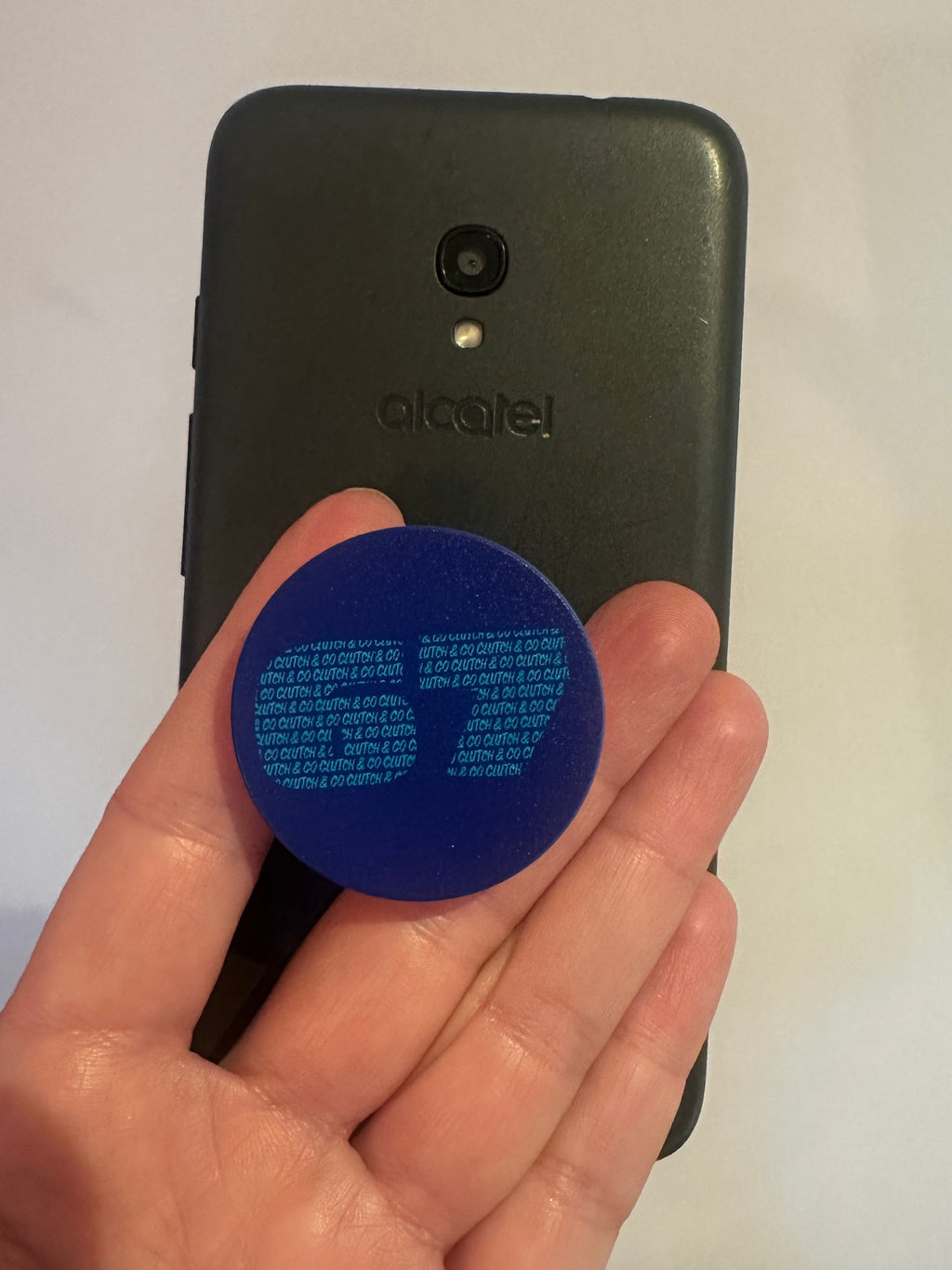 Hand holding a blue phone pop with Clutch and Co text in front of a black phone