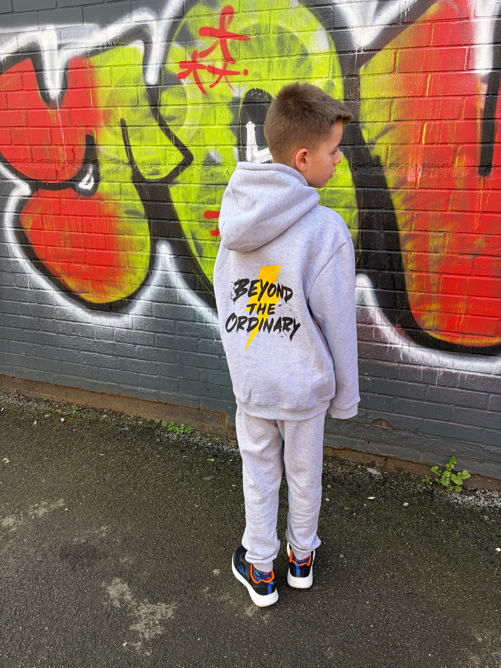 Person wearing a hoodie with text standing in front of a colorful mural.