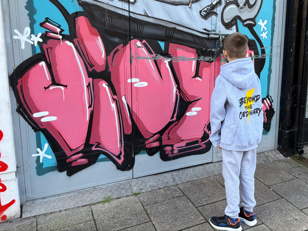 Person standing in front of a colorful mural on a door with graffiti-style text and abstract shapes.