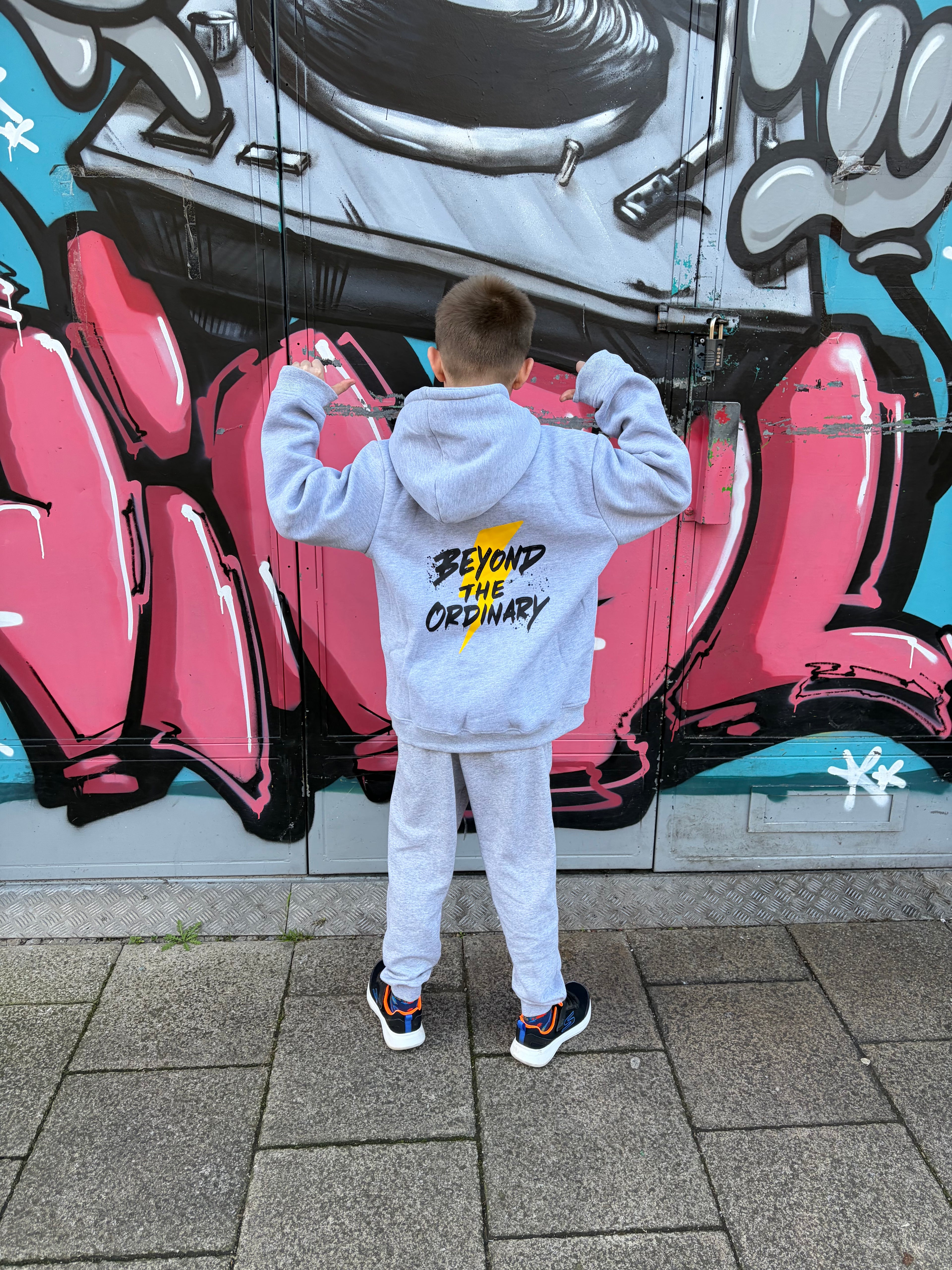 Person wearing a gray hoodie with text in front of a colorful mural.