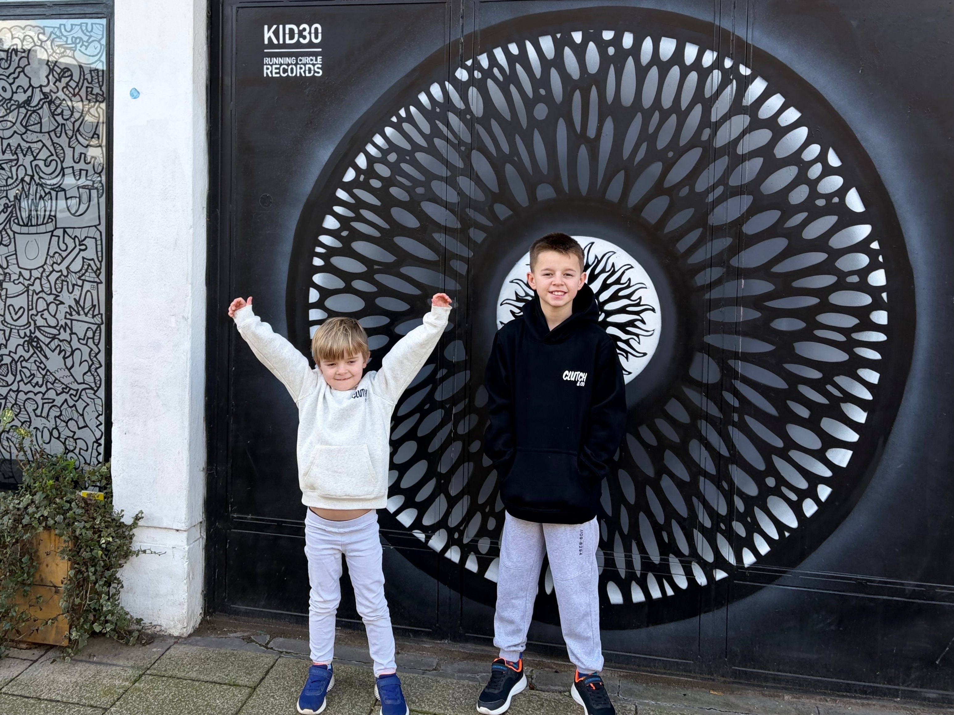 Two children standing in front of a decorative metal gate with 'KID30' branding.