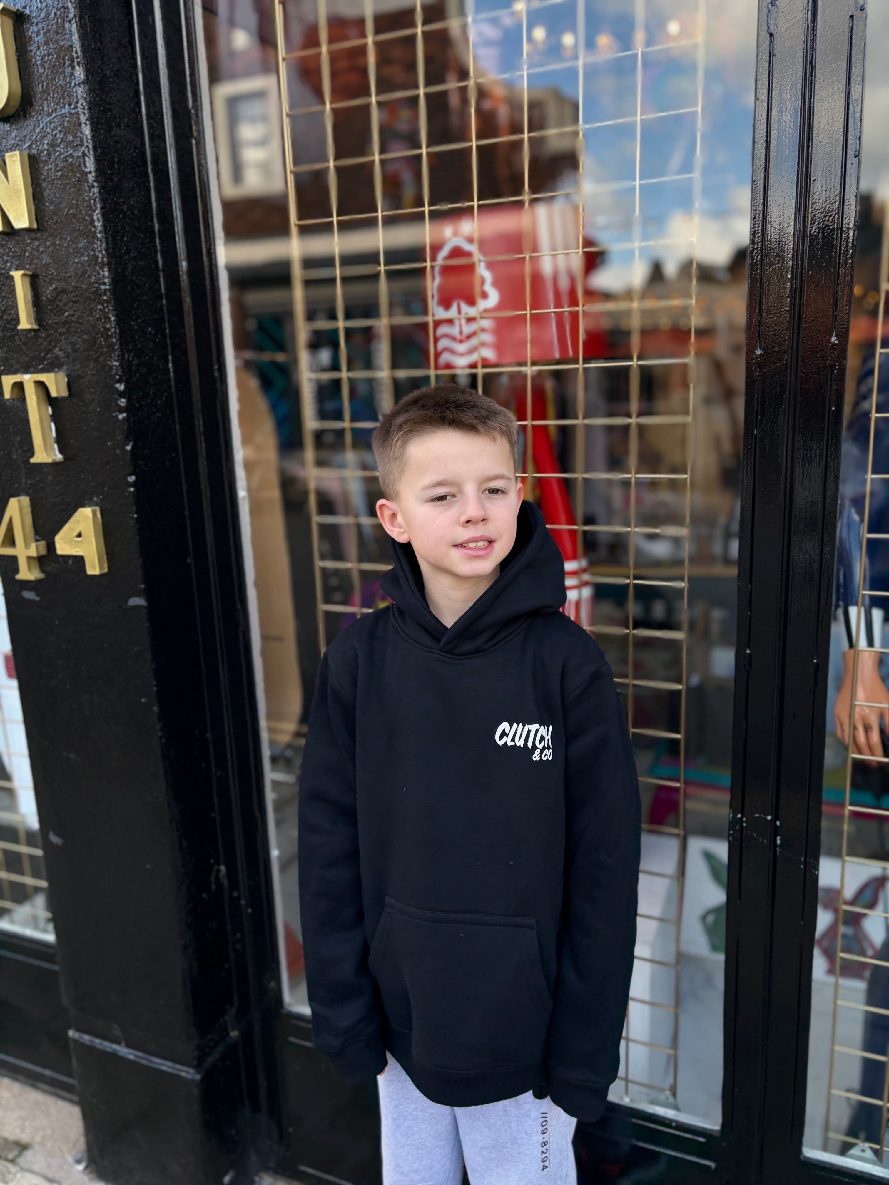 Child wearing a black hoodie with a logo standing in front of a store entrance.