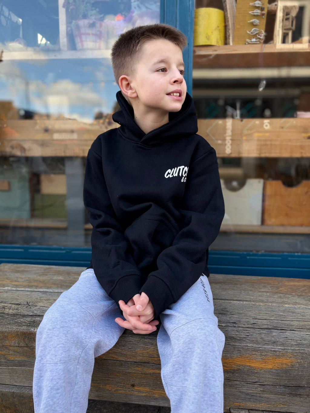 Child wearing a black hoodie with white text, sitting on a wooden bench.