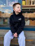Child wearing a black hoodie with white text, sitting on a wooden bench.