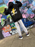 Person wearing a black hoodie with 'Beyond the Ordinary' text in front of a colorful graffiti wall.