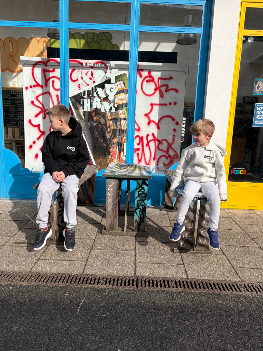 Two children sitting on a bench in front of a store with graffiti on the window.